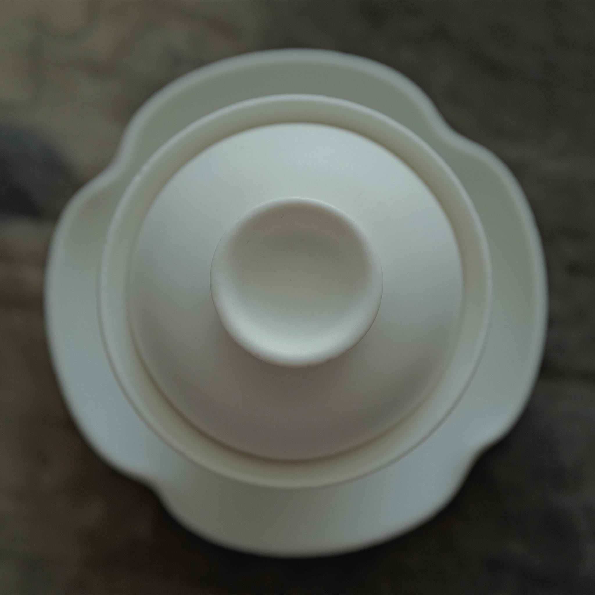 White ceramic gaiwan with lid on a matching saucer held by a hand.