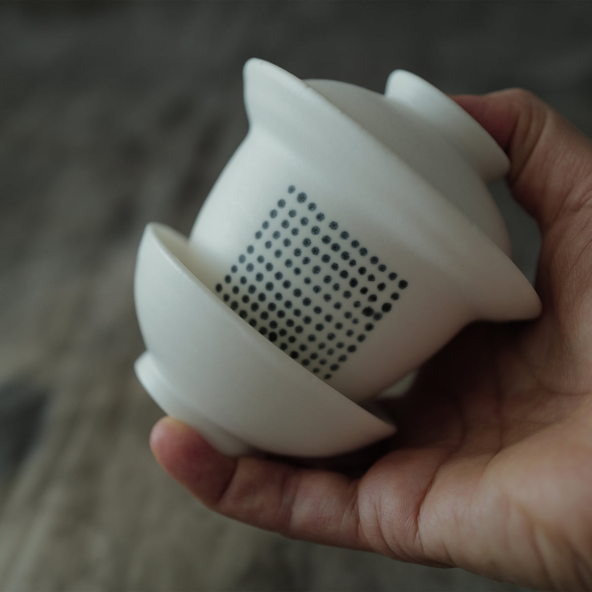 White ceramic gaiwan held in a hand with a blurred background.