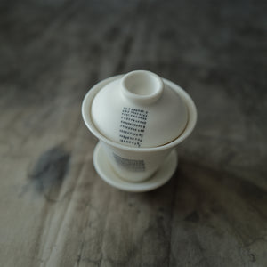 White ceramic gaiwan with lid on a textured surface.