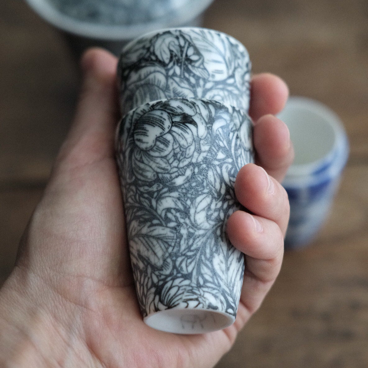 A hand holding two porcelain teacups with a peony floral pattern