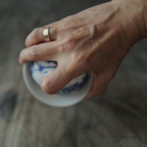 Hand holding a blue and white ceramic gaiwan with floral patterns against a blurred background.