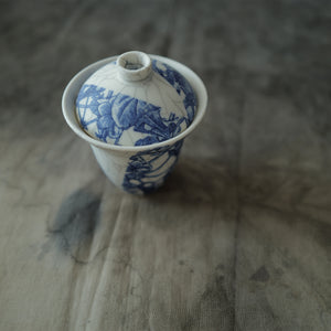 Blue and white ceramic gaiwan  with floral patterns on a textured surface.