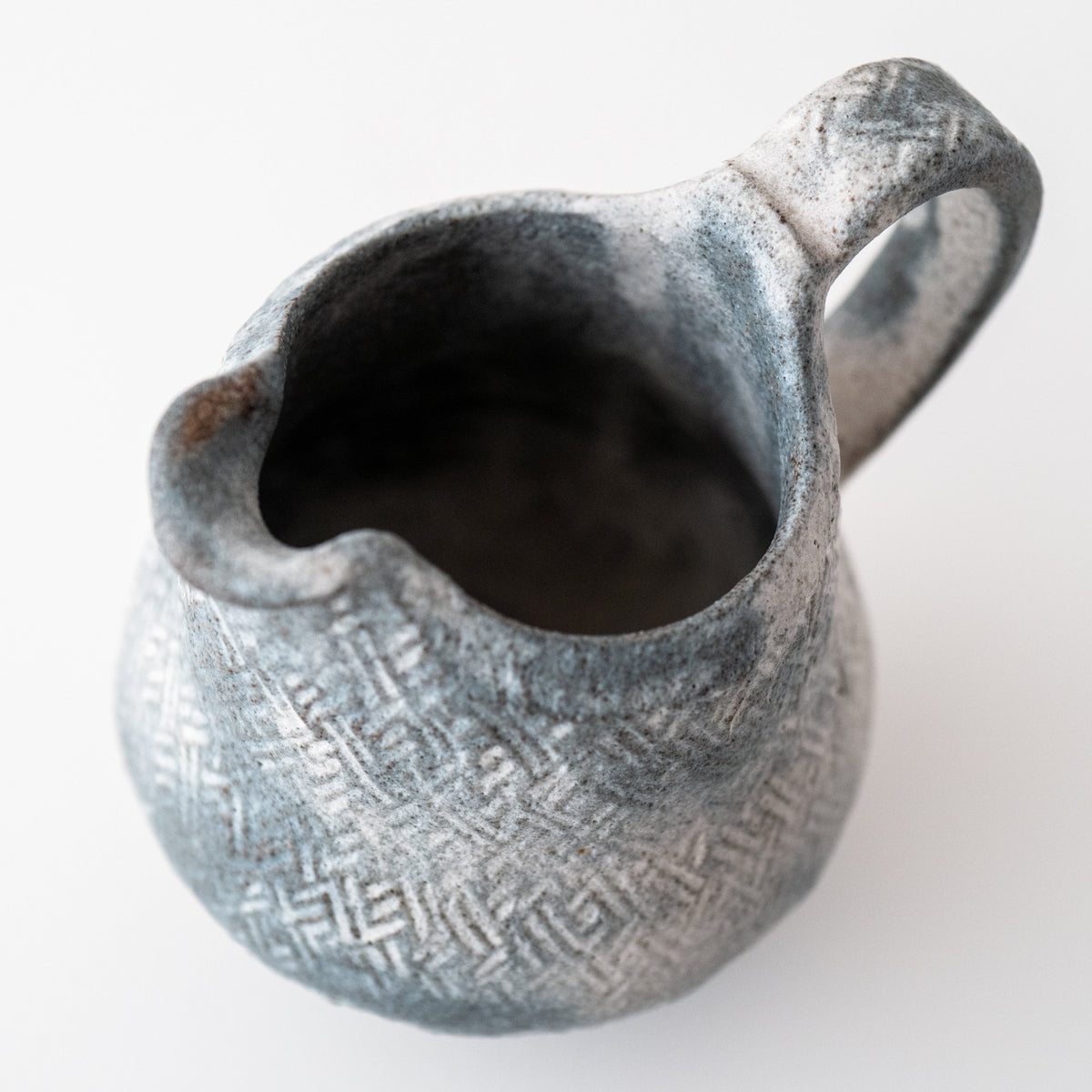 A hand-built stoneware pitcher with a matte glaze, decorated with a wooden roller, featuring a geometric pattern.