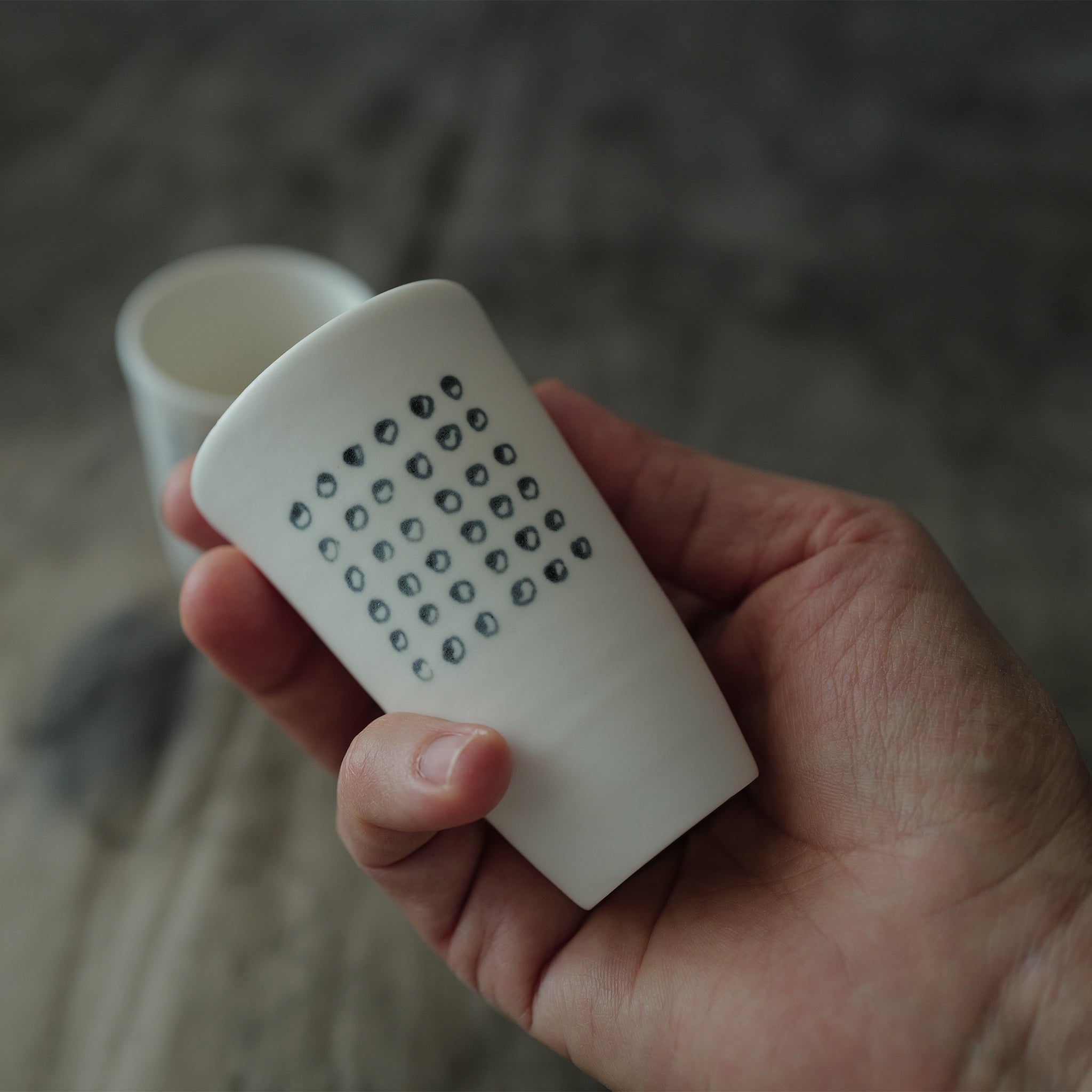 Hand holding a white teacup with a pattern on a blurred background.
