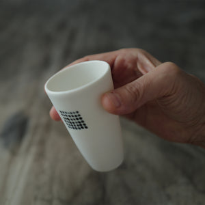 Hand holding a white ceramic teacup on a blurred background.