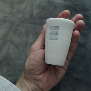 Hand holding one white  teacup with a textured surface against a blurred background.