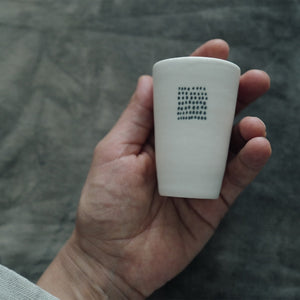 Hand holding one white  teacup with a textured surface against a blurred background.